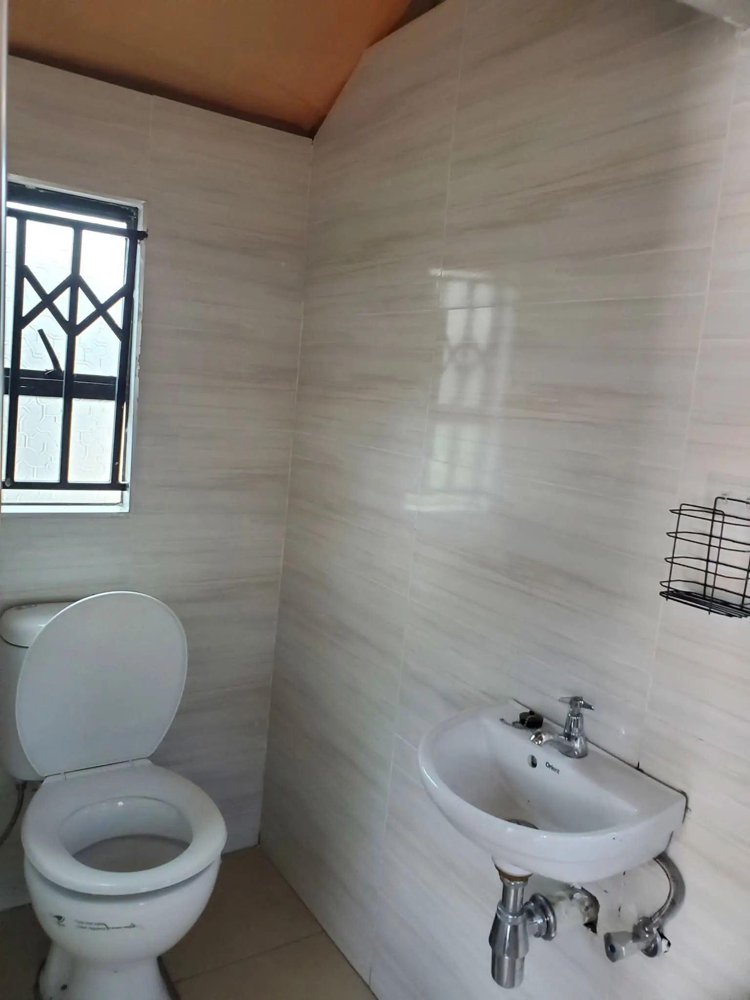 Tiled private bathroom with toilet, basin and window
