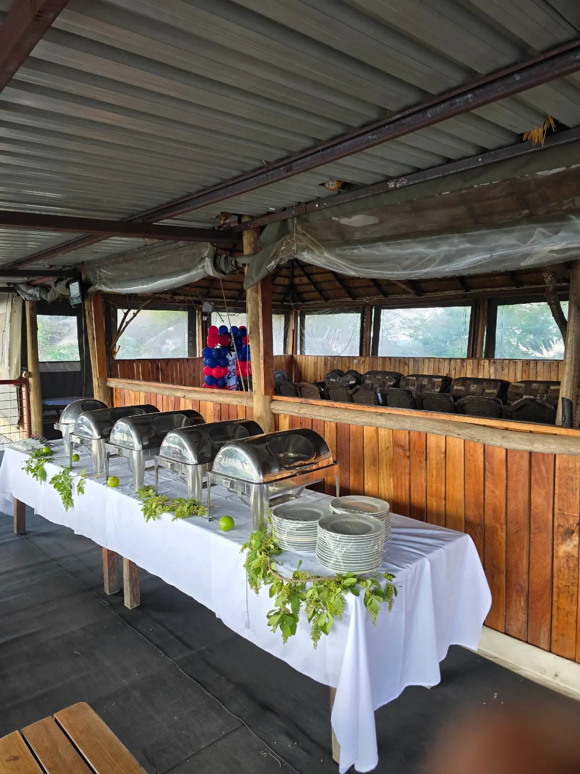 Buffet of chafing dishes and plates set up in a covered outdoor area