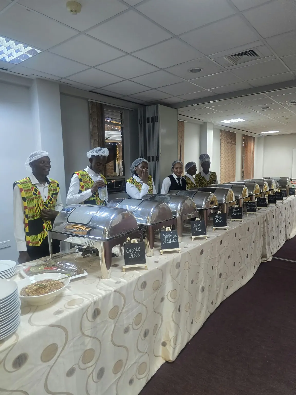 Resort staff in patterned vests serving a group buffet from a long table