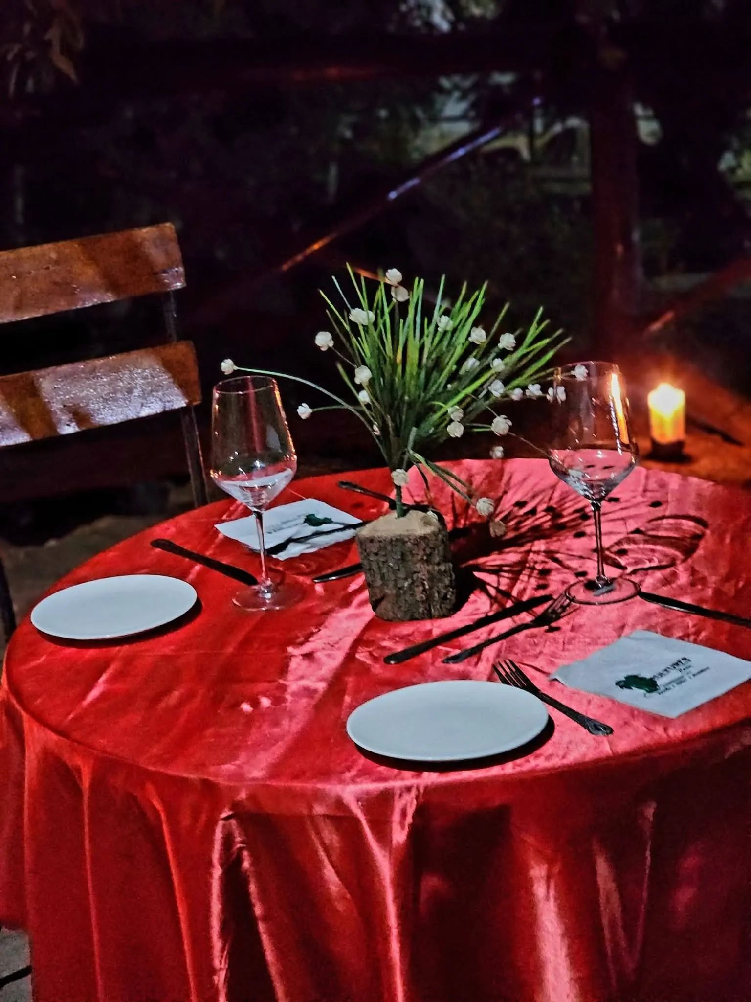 Outdoor dinner table with a red cloth, wine glasses and a candle at night