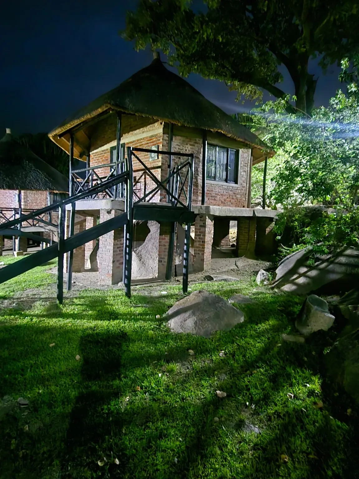 Thatched chalet with an outdoor staircase, lit among trees at night