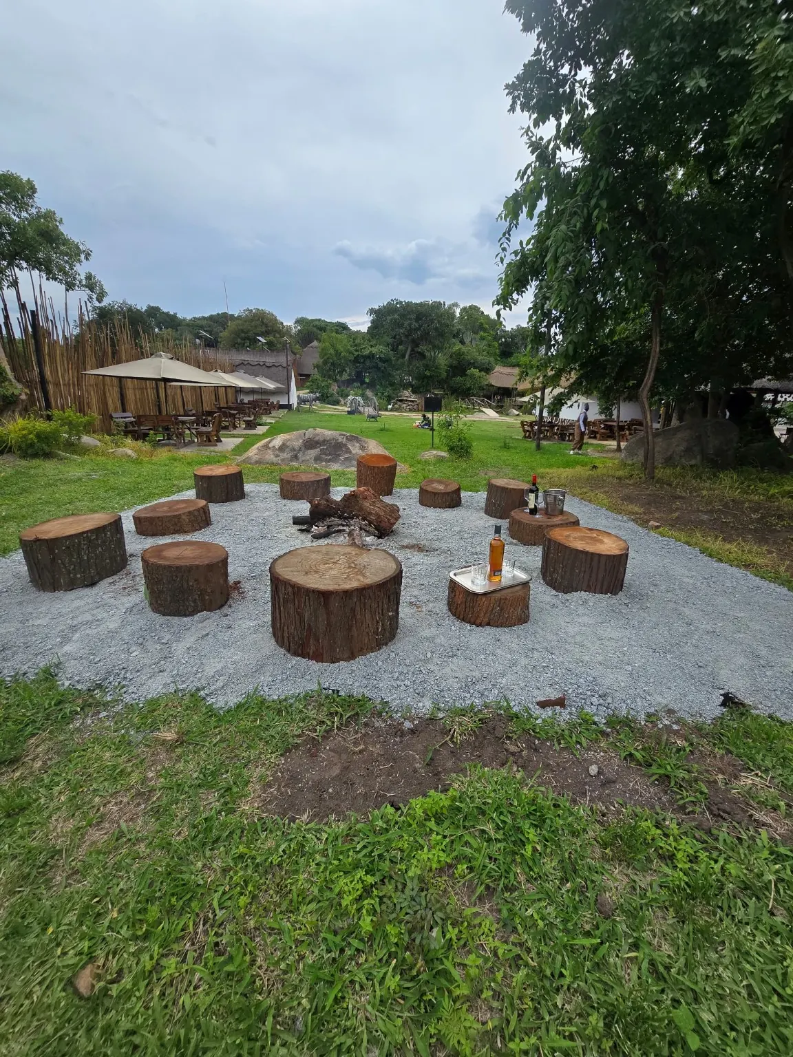 Circle of log stools around a fire pit on gravel, with the resort grounds behind