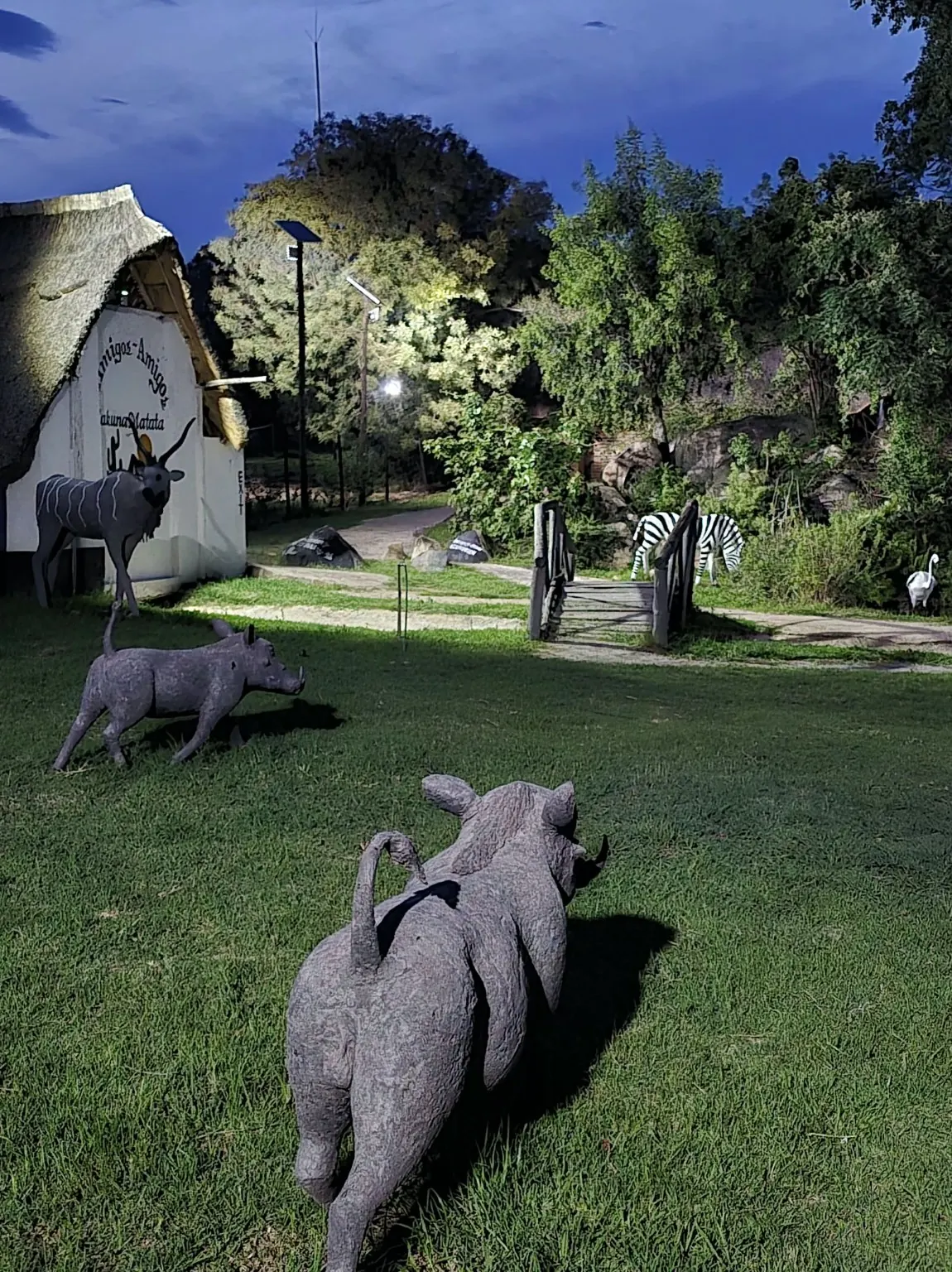 Resort lawn at dusk with metal animal sculptures, trees and thatched buildings
