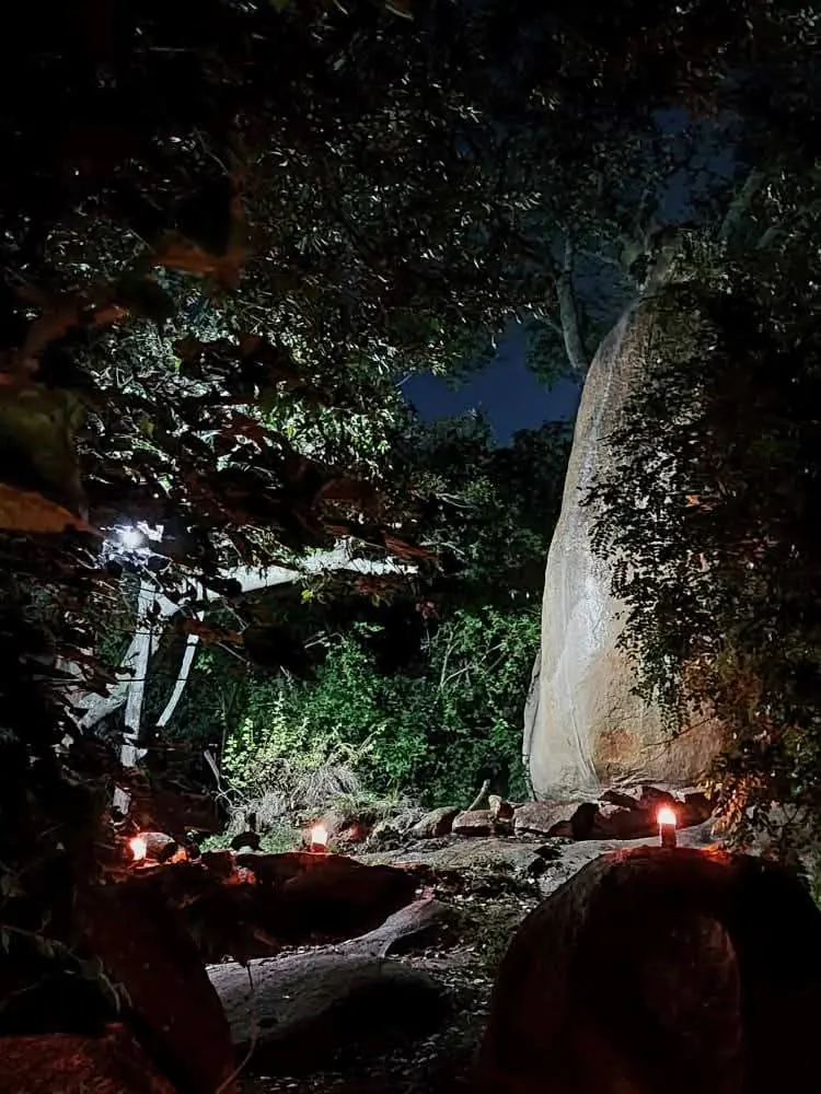 Large boulder among trees at night, lit with small candles