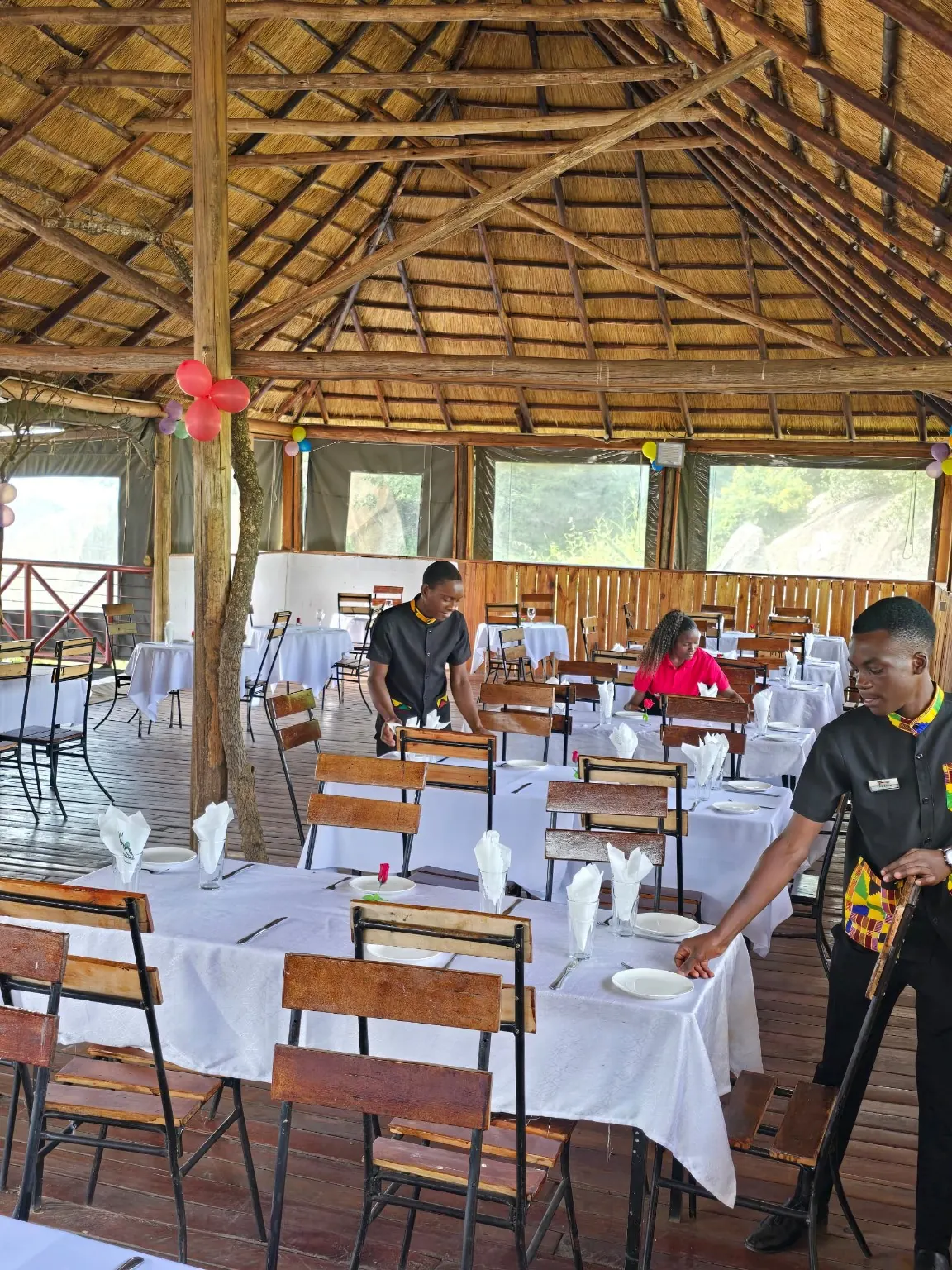 Staff laying tables in a thatched, open-sided dining pavilion