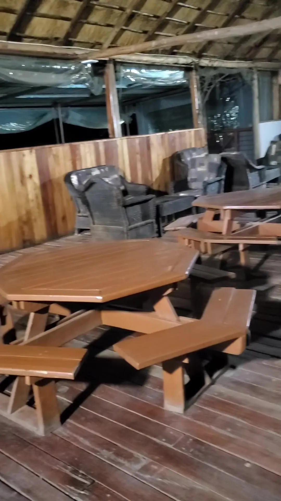 Octagonal wooden picnic tables on a timber deck under a thatched roof, with lounge chairs beyond