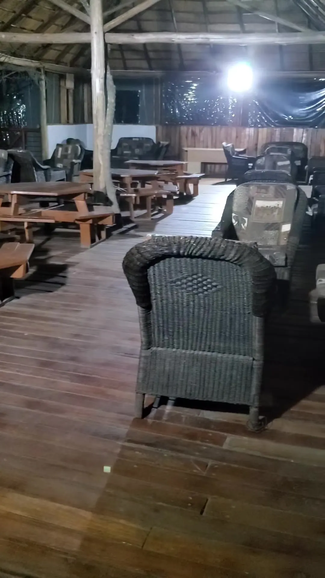 Wicker lounge chairs and wooden tables under a thatched roof at night