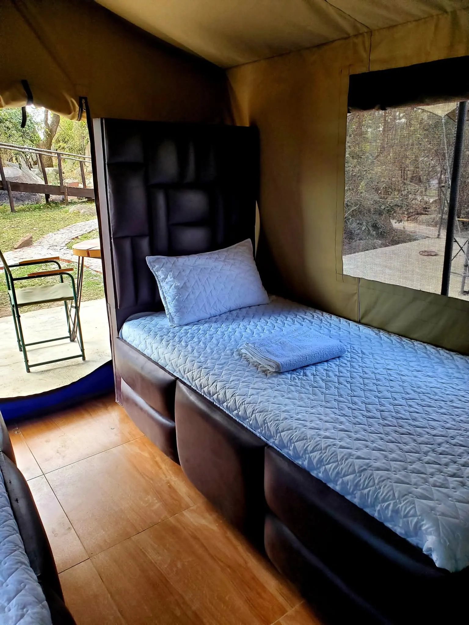 Inside a tented room: a made bed beside a window with a view of the grounds