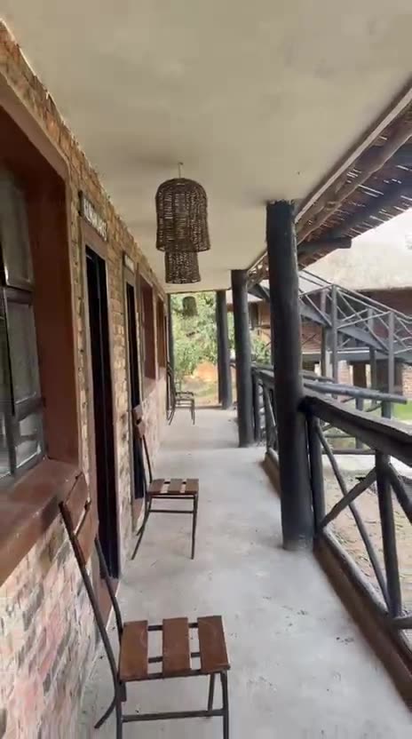 The upstairs walkway of the brick and thatch chalets, with room doors on one side, a railing and wooden chairs