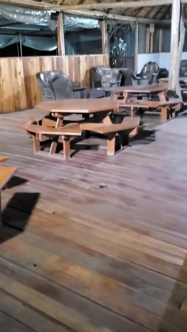 Walkthrough of the covered deck: wooden picnic tables, wicker lounge chairs and red railings