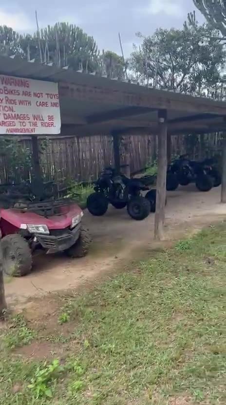 Quad bikes parked under a covered shelter beside the lawn, with a rules sign on the post