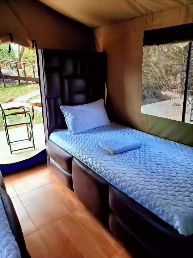 Walkthrough of a tented room: beds, wooden floor and the bathroom doorway